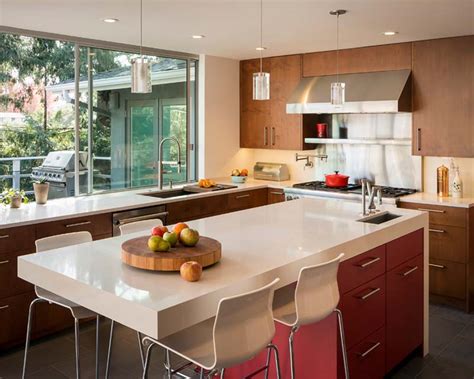 A stainless steel hood is suspended from the ceiling which hangs over a kitchen island topped with a stainless steel counter fitted with a freestanding stove next to a. 6 Top Spots for a Second Kitchen Sink