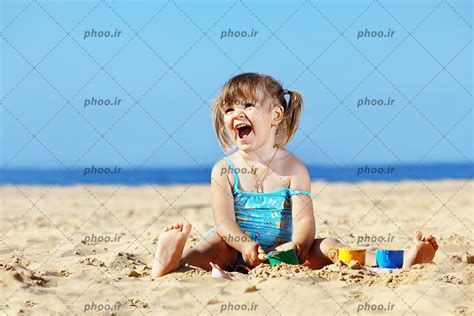 عکس با کیفیت دختر بچه شاد در حال بازی با ماسه ها در پس زمینه آبی عکس با کیفیت و تصاویر استوک