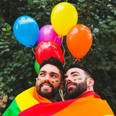 casal gay feliz com balões lgbt abraçando no jardim foto grátis