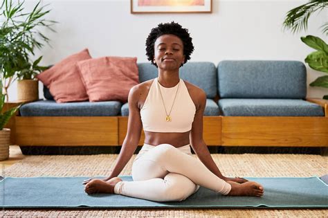 An Attractive Young Black Woman Sitting On A Yoga Mat In Her Lounge At Home Meditating In 2021