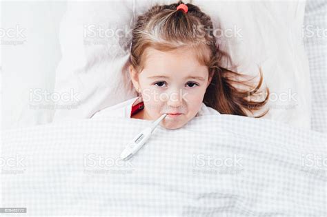 Sick Girl With A Thermometer In Mouth Lying In Bed Stock Photo