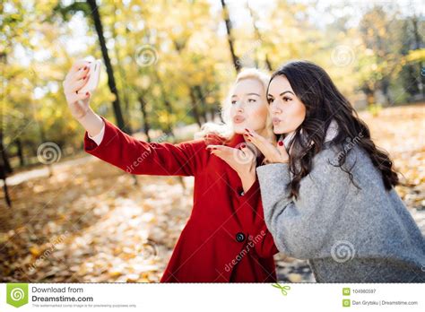 Two Beautiful Girls Making Selfie And Blow Kiss In Autumn Park Stock