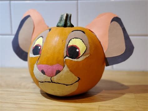 A Pumpkin Decorated To Look Like A Mouses Head On A Wooden Table In
