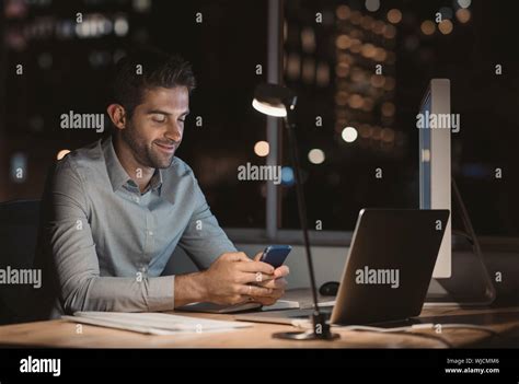 Smiling Young Businessman Reading A Text Message While Working Late