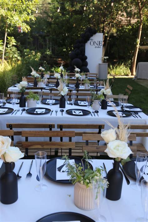 The Table Is Set With Black And White Plates Napkins And Vases