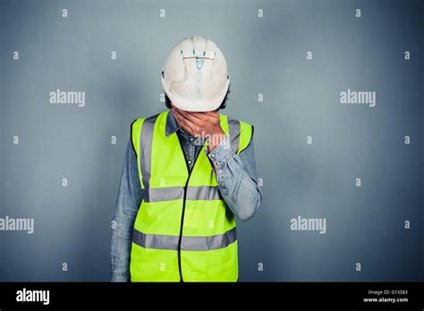 A Young Engineer Wearing A High Vis Vest And Hard Hat Is Covering His