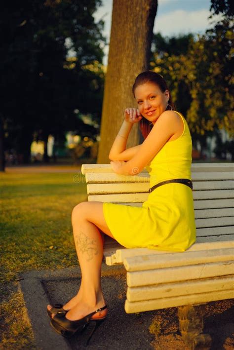 Attractive Young Woman In Yellow Dress Sitting In A Summer Park On A