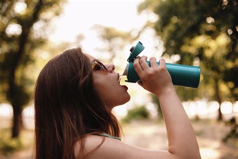 Young Woman Drinking Water From Reusable Bottle In Summer Park