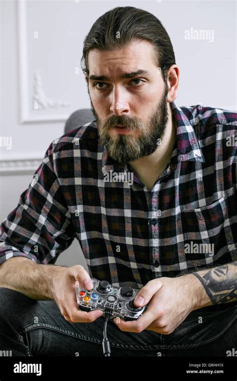 A Young Hipster With Beard Plays A Video Game Seated With Strength In