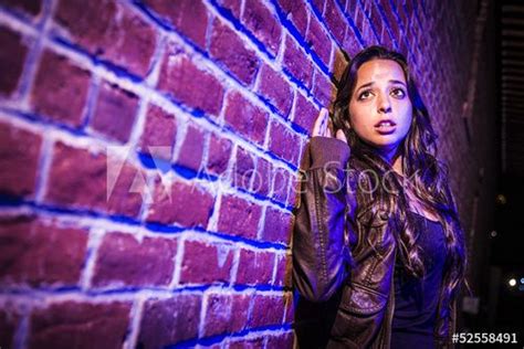 Frightened Pretty Young Woman Against Brick Wall At Night