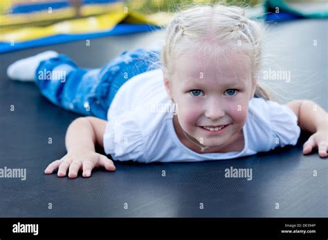 Pretty Little Blond Girl Lying On Her Stomach On A Trampoline Lifting Her Head To Smile Happily