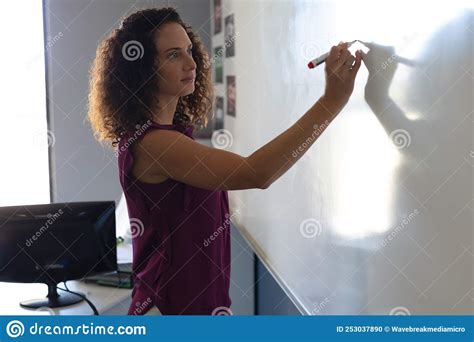 Side View Of Caucasian Young Female Teacher Writing On Whiteboard