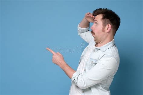 Young Man Pointing Surprised By Something Or Someone Isolated On Blue
