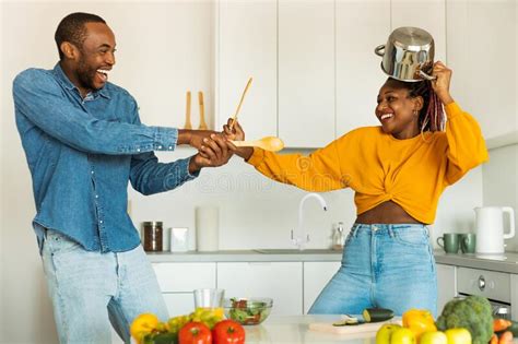 domestic fun playful black couple fighting in kitchen using spatulas as a weapons fooling