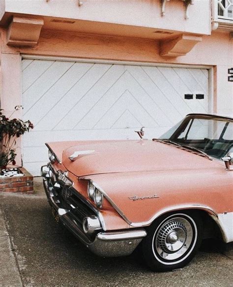 An Old Pink And White Car Parked In Front Of A House With A Garage Door