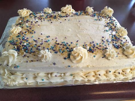 A Cake With White Frosting And Sprinkles On It Sitting On A Table