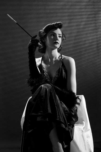 A Woman Sitting On Top Of A White Chair Holding A Cane In Her Hand And Wearing A Black Dress