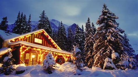 Cabin In The Snow With Christmas Lights At Night And Snow Covered