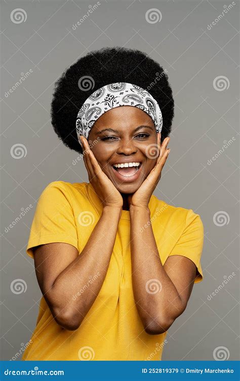 Cheerful African American Woman With Headband Fixing Kinky Hair Puts Hands On Face Smiling Stock