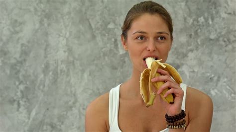 Young Woman Holding Banana Eating It Looking At Camera