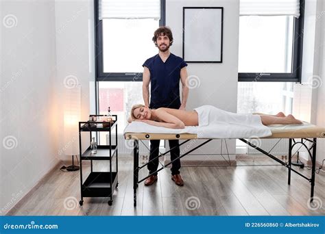 Caucasian Male Massage Therapist Stands Next To Client Lying On Massage