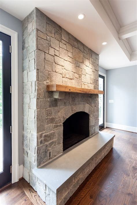A Stone Fireplace In The Middle Of A Room With Wood Flooring And Large