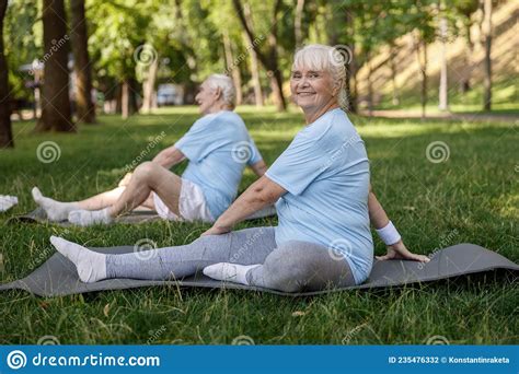 Positive Mature Woman With Friend Do Yoga Asanas On Field Grass In