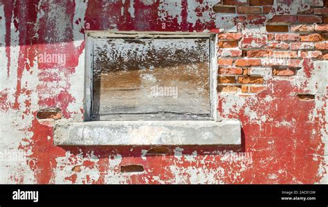 Boarded Up Window In A Crumbling Wall Of An Abandoned Building With Red