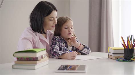 Side View Of Brunette Caucasian Mother Helping Daughter To Write Down