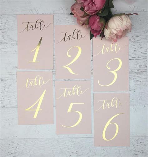 Pink And Gold Wedding Table Numbers With White Calligraphy On The Front