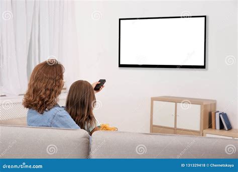 mother and daughter with remote control sitting on couch and watching