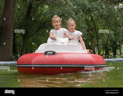 Two Tween Girls Riding On Red Inflatable Motorboat In Fun Park Stock