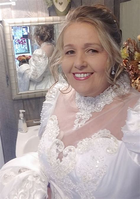 A Woman In A Wedding Dress Is Smiling At The Camera While Standing Next To A Mirror