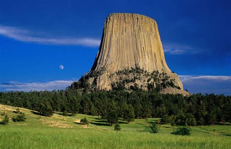 A Tall Rock Formation Towering Over A Lush Green Field Under A Blue Sky