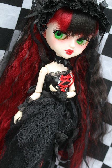 A Doll With Red Hair And Green Eyes Is Sitting On A Checkerboard Floor