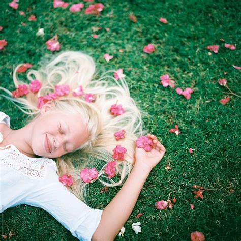 blonde girl laying in green grass with pink flowers by stocksy contributor wendy laurel