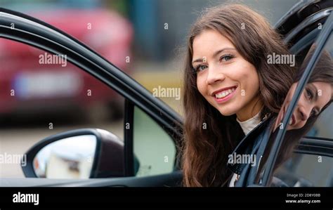 Young Smiling Woman Sits In A Car With An Open Door And Looks Back