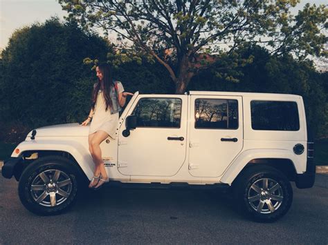 A Woman Sitting On Top Of A White Jeep Parked In A Parking Lot Next To