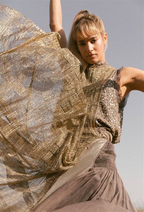 A Woman Is Posing With Her Dress Blowing In The Wind And Holding It