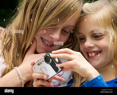Two Young Girls Sisters Smiling While Looking At Pictures On Their