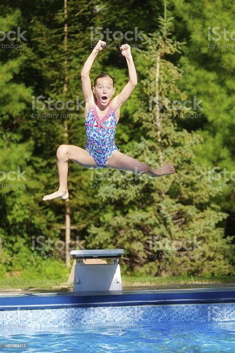 Young Girl Jumping Off Diving Board Into Summer Swimming Pool Stock