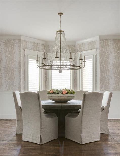 Clear Beaded Chandelier Over A Round Wood Dining Table With Gray Linen