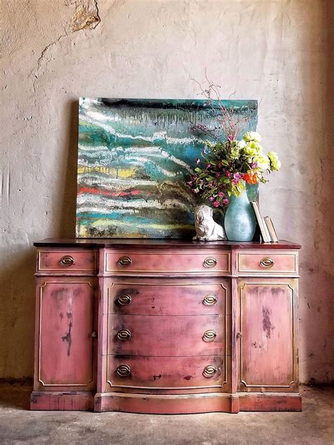 An Old Dresser With Flowers On Top And A Painting In The Corner Behind