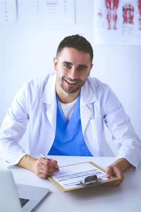 Portrait Of A Male Doctor With Laptop Sitting At Desk In Medical Office