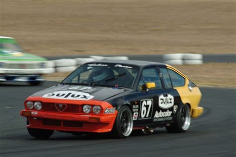 An Orange And Black Car Driving On A Race Track With Another Car Behind