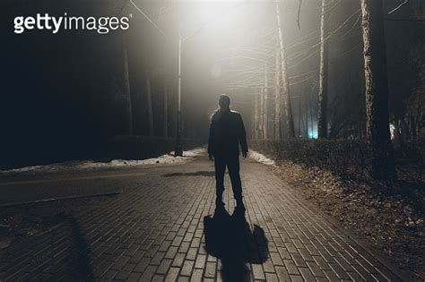 Sad Man Alone Walking Along The Alley In Night Foggy Park Back View