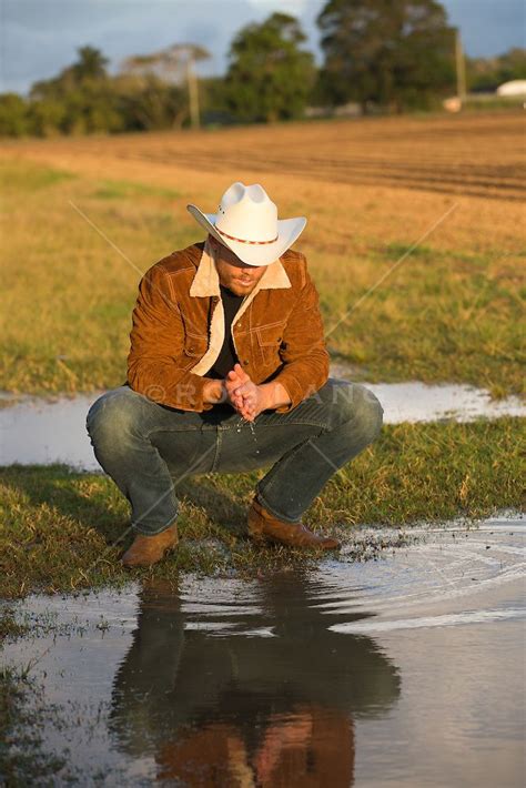 Cowboy Kneeling Down To Gather Water From A Pond On A Ranch Cowboy