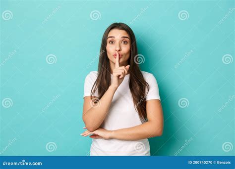 Portrait Of Cute Brunette Girl In White T Shirt Hushing With Finger Over Lips Telling A Secret