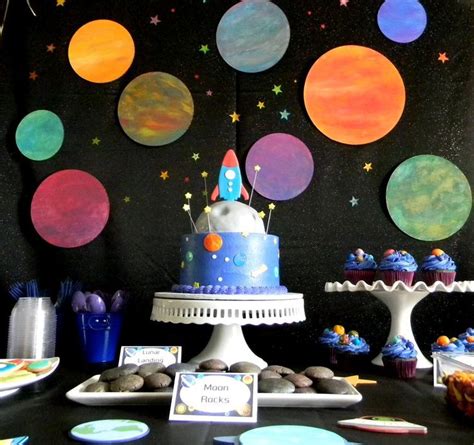 A Space Themed Birthday Party With Cake And Cupcakes On A Table In Front Of An Outer Planets