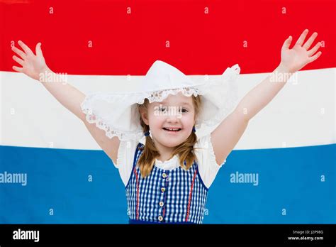 Little Dutch Girl Wearing Traditional National Costume Dress And Hat With Flag Of The